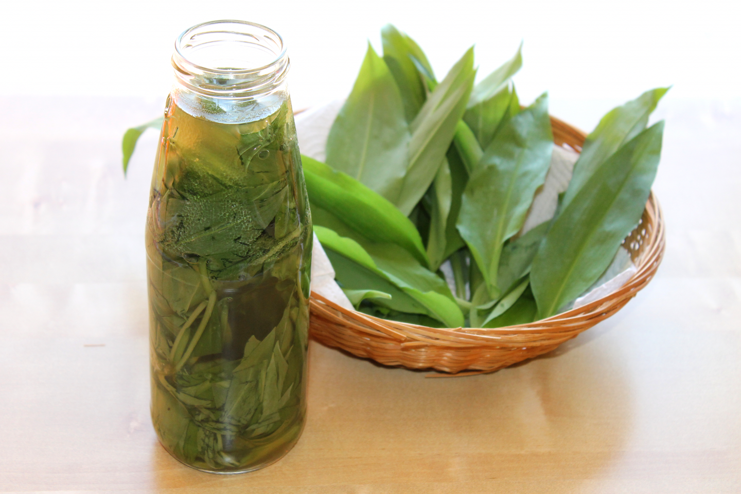 Selbstgemachter Bärlauchessig mit frischen Bärlauchblättern in der Flasche, daneben Körbchen mit frischen Bärlauchblättern