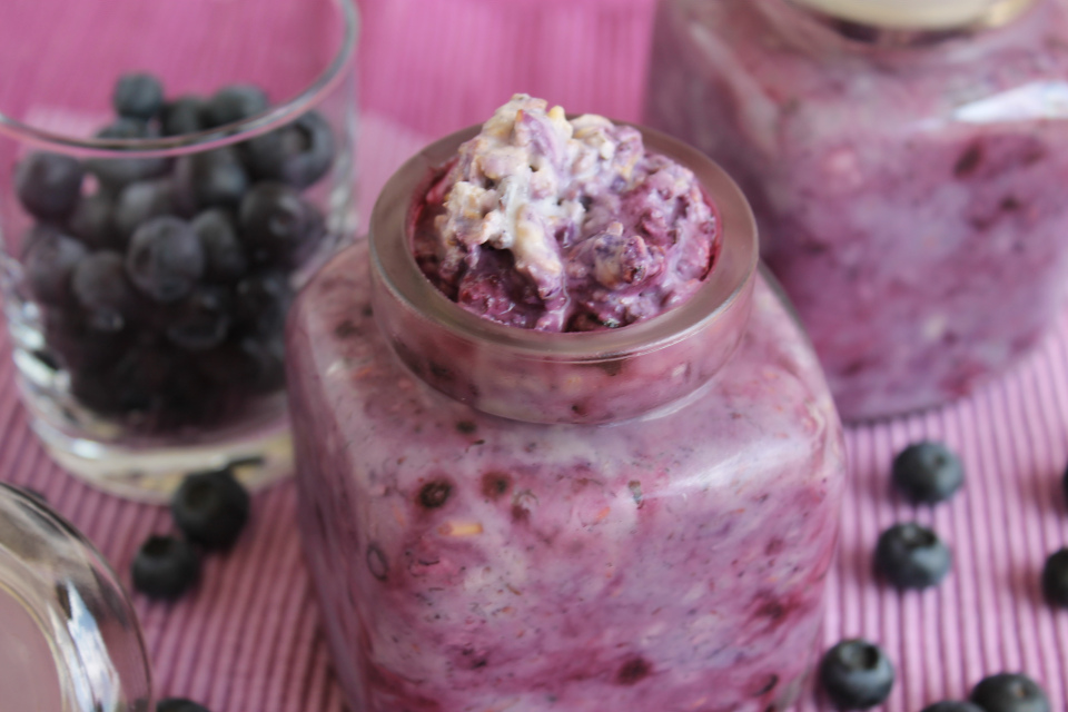 Nahaufnahme zwei gefüllte Einmachgläser mit veganen Heidelbeer-Kokos Overnight Oats, daneben Glas mit frischen Heidelbeeren
