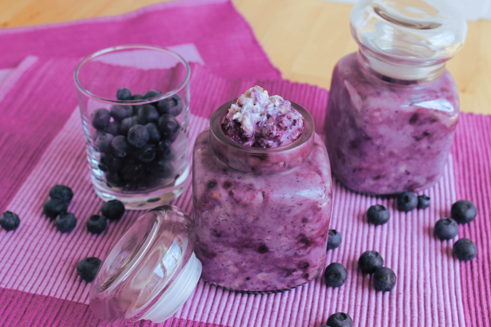 Zwei gefüllte Einmachgläser mit veganen Heidelbeer-Kokos Overnight Oats, daneben Glas mit frischen Heidelbeeren